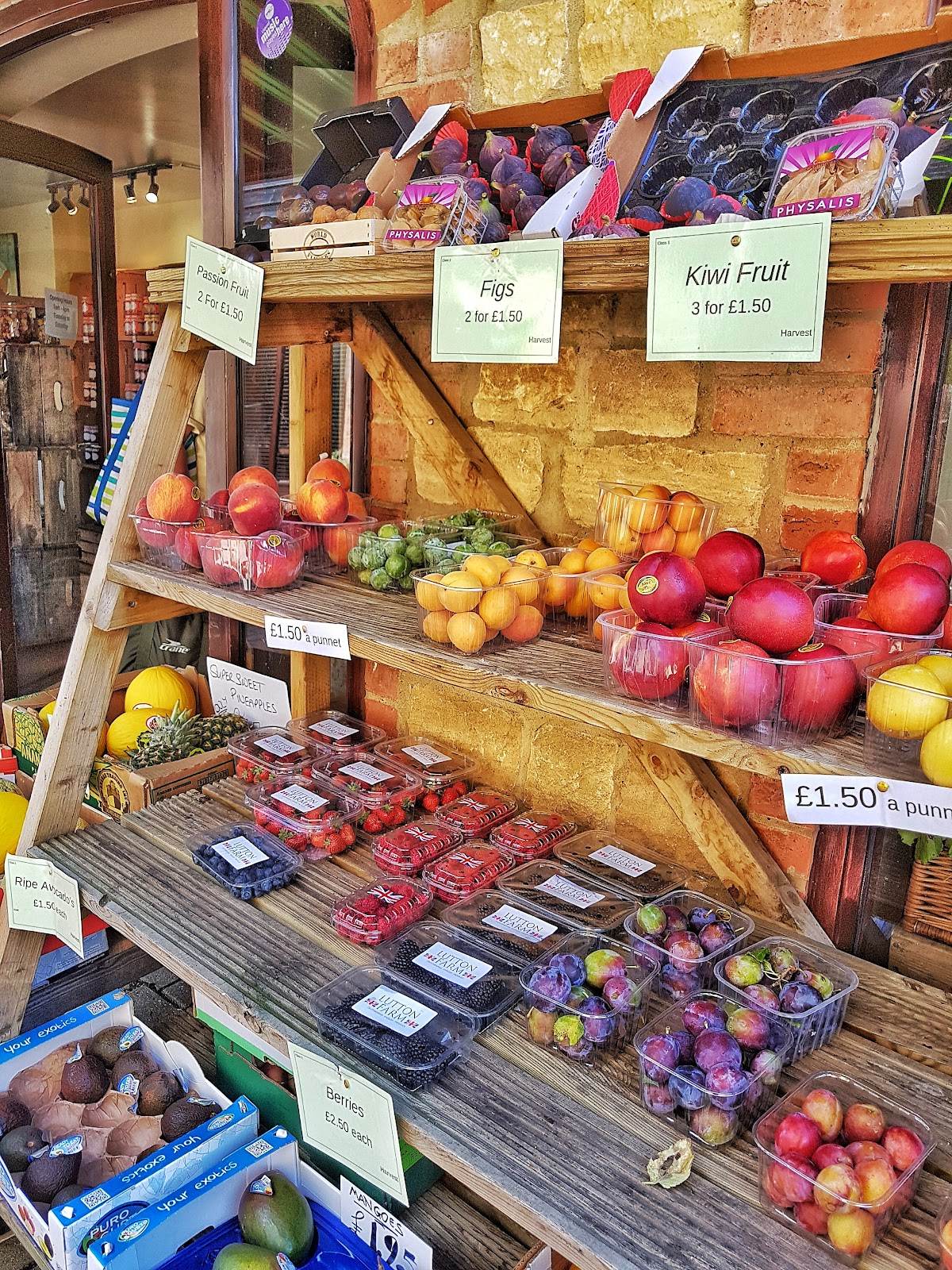 A wooden ladder shelf stacked with punnets of berries, plums, figs and apples, each labelled with a pale green Harvest ticket