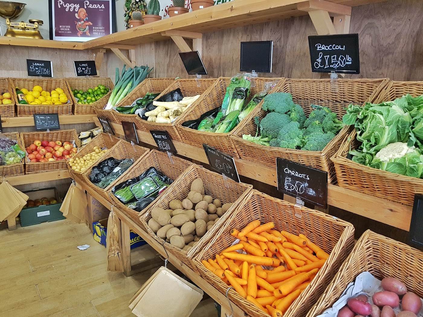 Rows of wicker baskets inside the shop holding carrots, potatoes, broccoli, leeks and lettuces under chalkboard signs