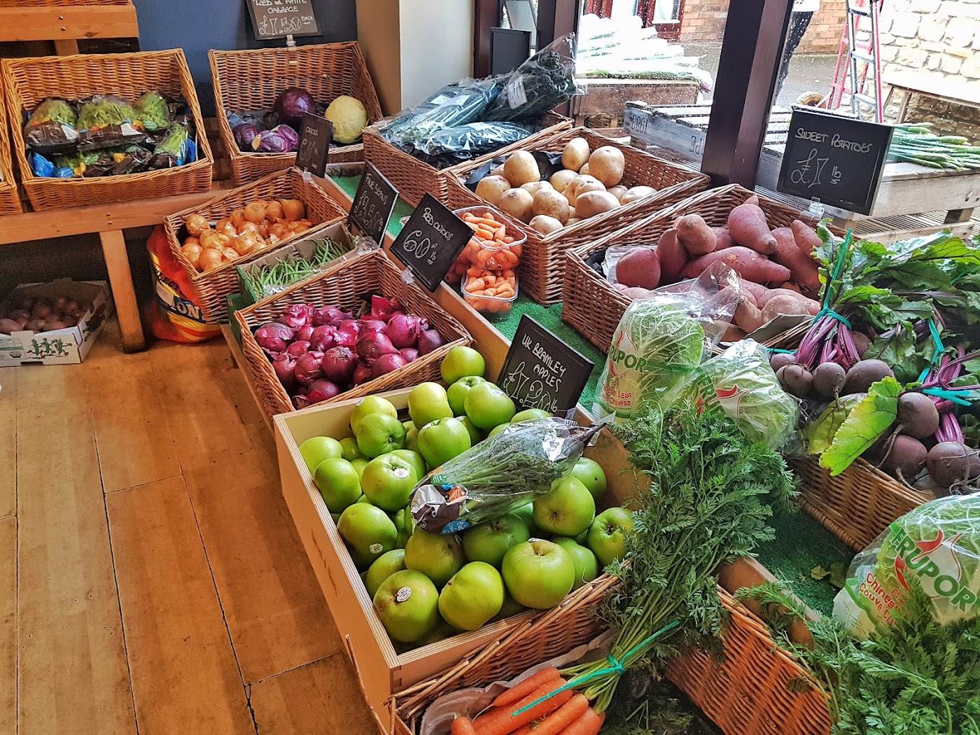 Baskets and crates of apples, beetroot, sweet potatoes, red onions and bunched carrots indoors